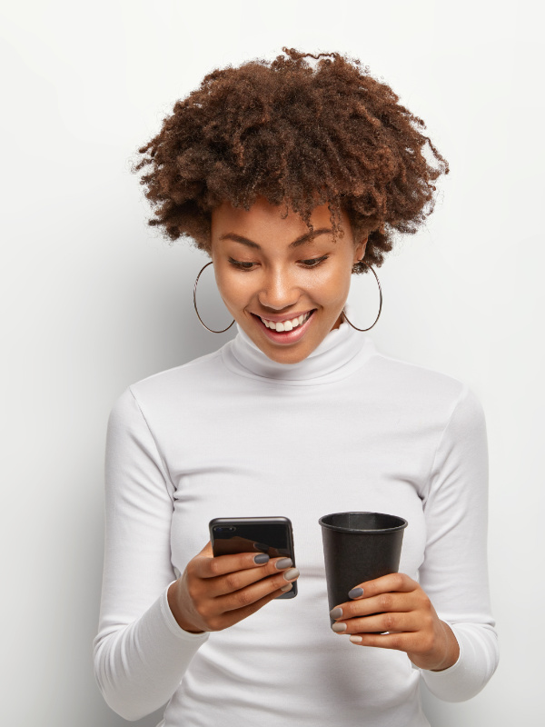 Jolie Jeune femme afro profitant du wifi avec son téléphone mobile avec un café